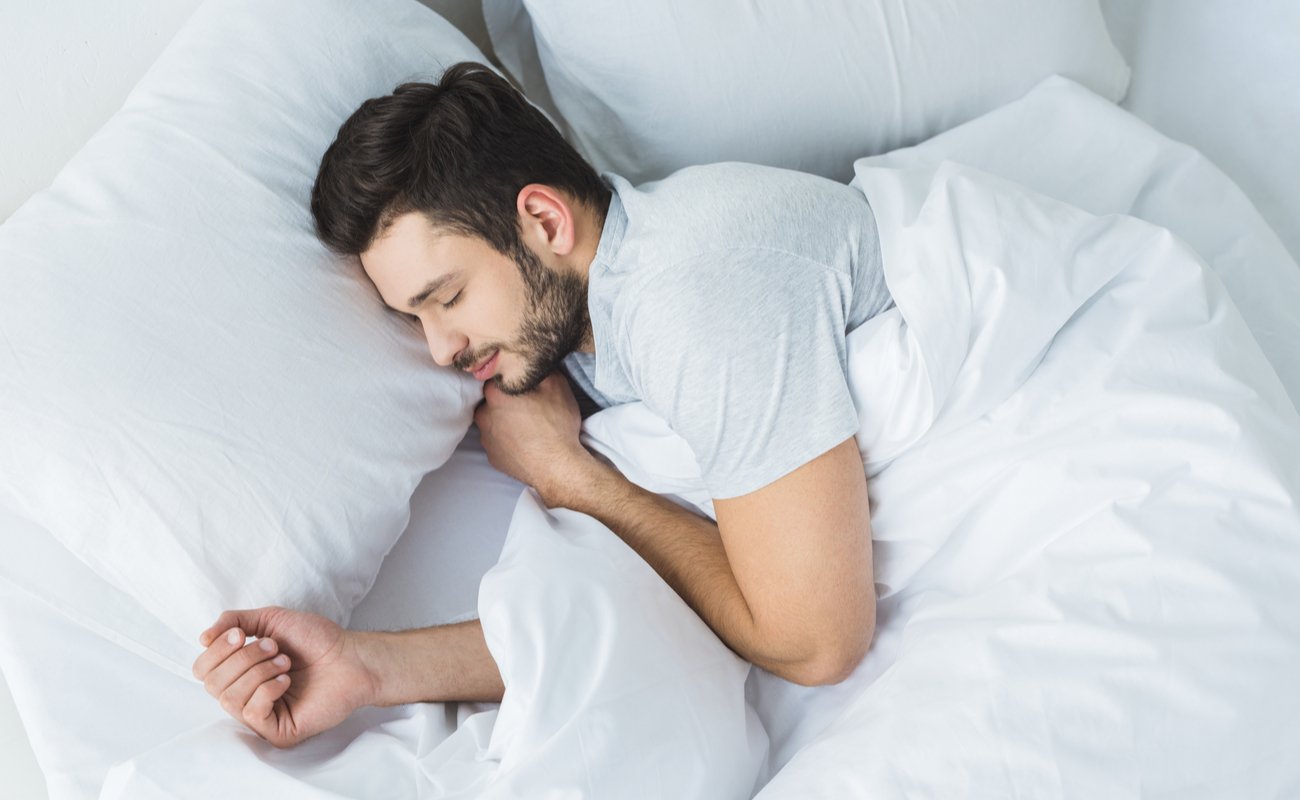 Man happily sleeping in a white bed
