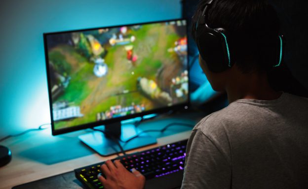 A guy playing an online game on his PC with a headset on