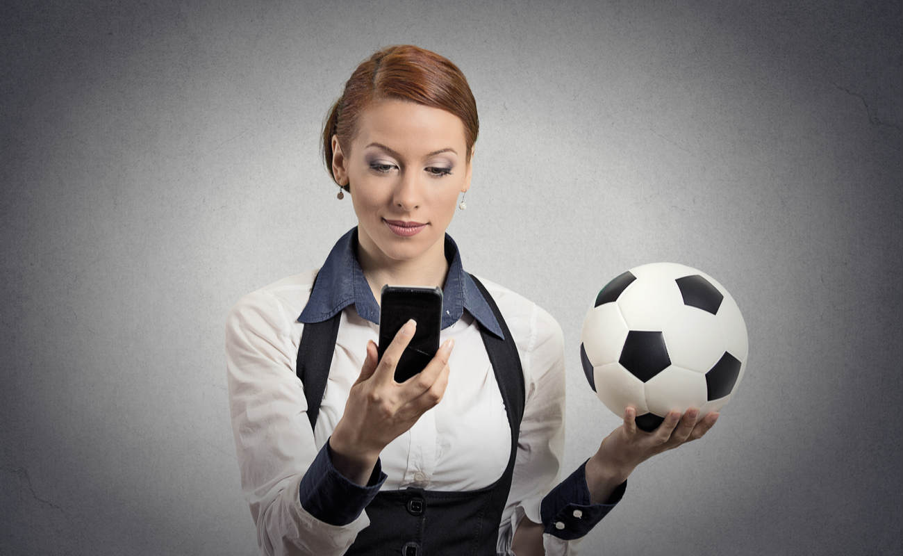 Woman holding a ball reads something on her phone looking smart. 