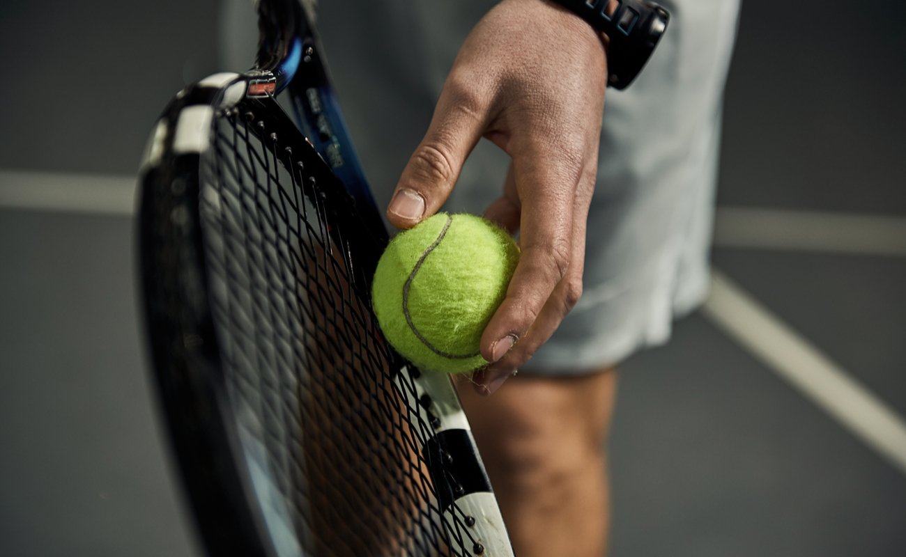 Close-up of male hand holding a tennis ball and racket