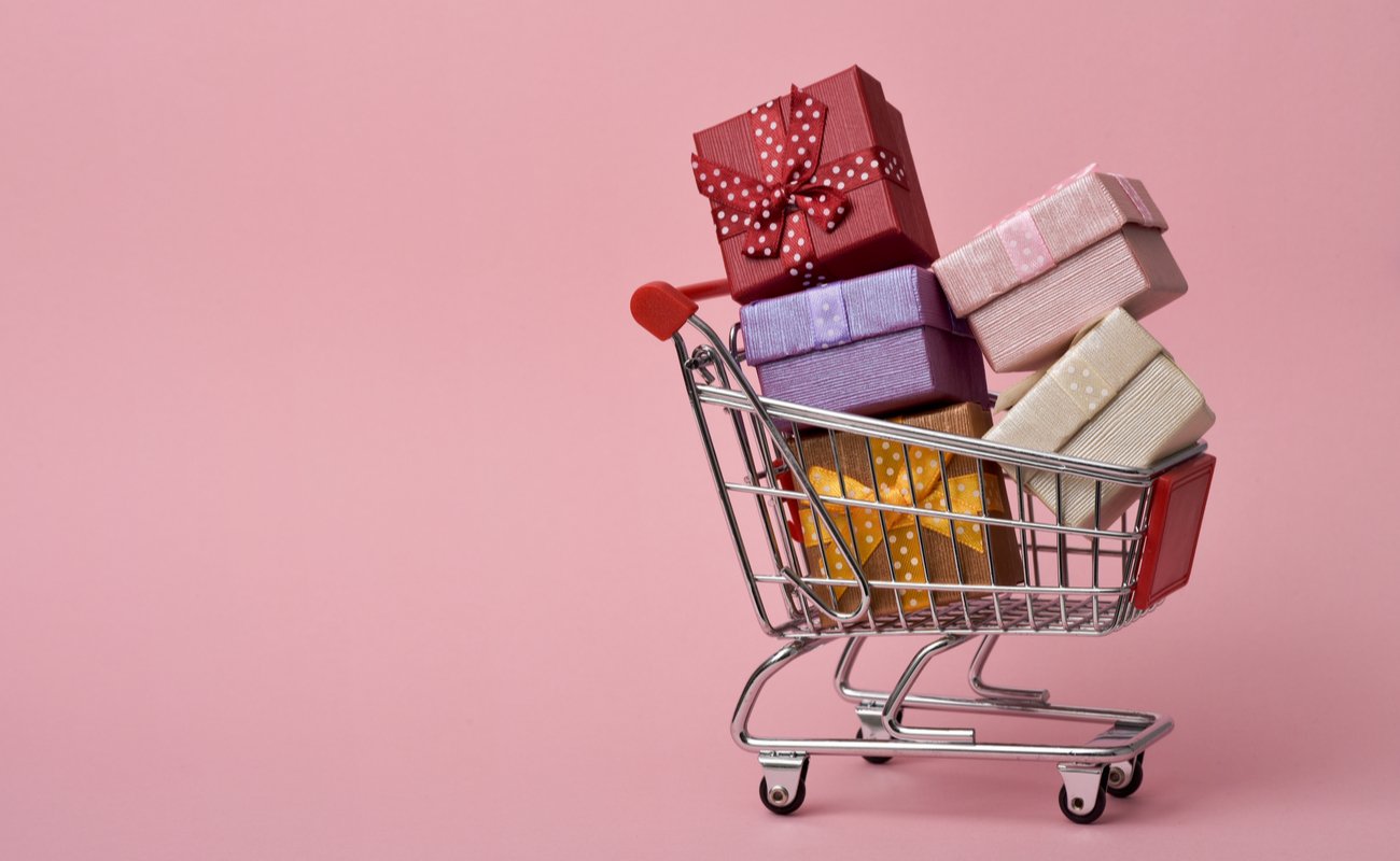 Mini gifts stacked up in a mini trolley in front of a pink background