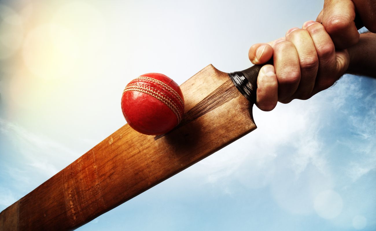 Cricket batsman hitting a ball shot from below against a blue sky