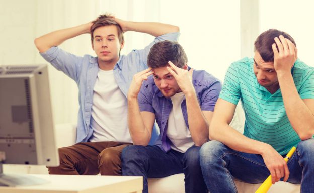 Sad male friends watching sports on tv at home