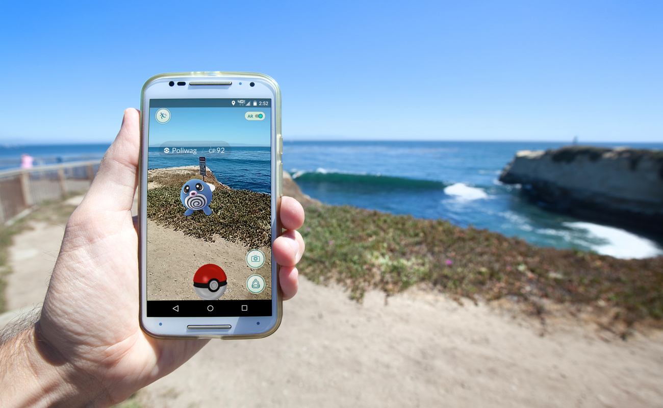 Someone holding a phone whilst playing Pokemon Go by the sea