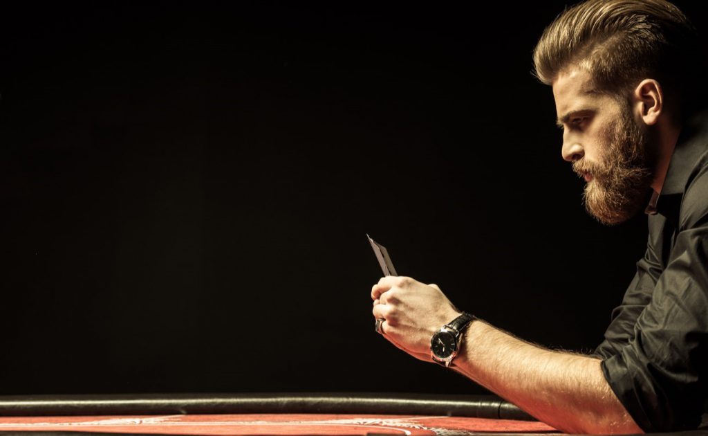 Side view of bearded man holding poker cards isolated on black
